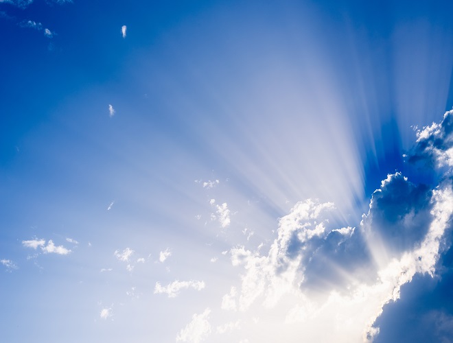 Sunbeams rising from a large cloud in intense blue sky on a summ