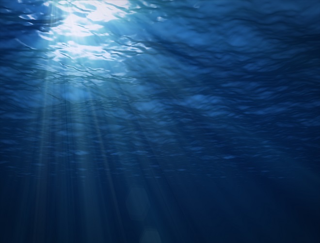 The rays of the sun make their way to the depths through the surface of the water. Underwater background.